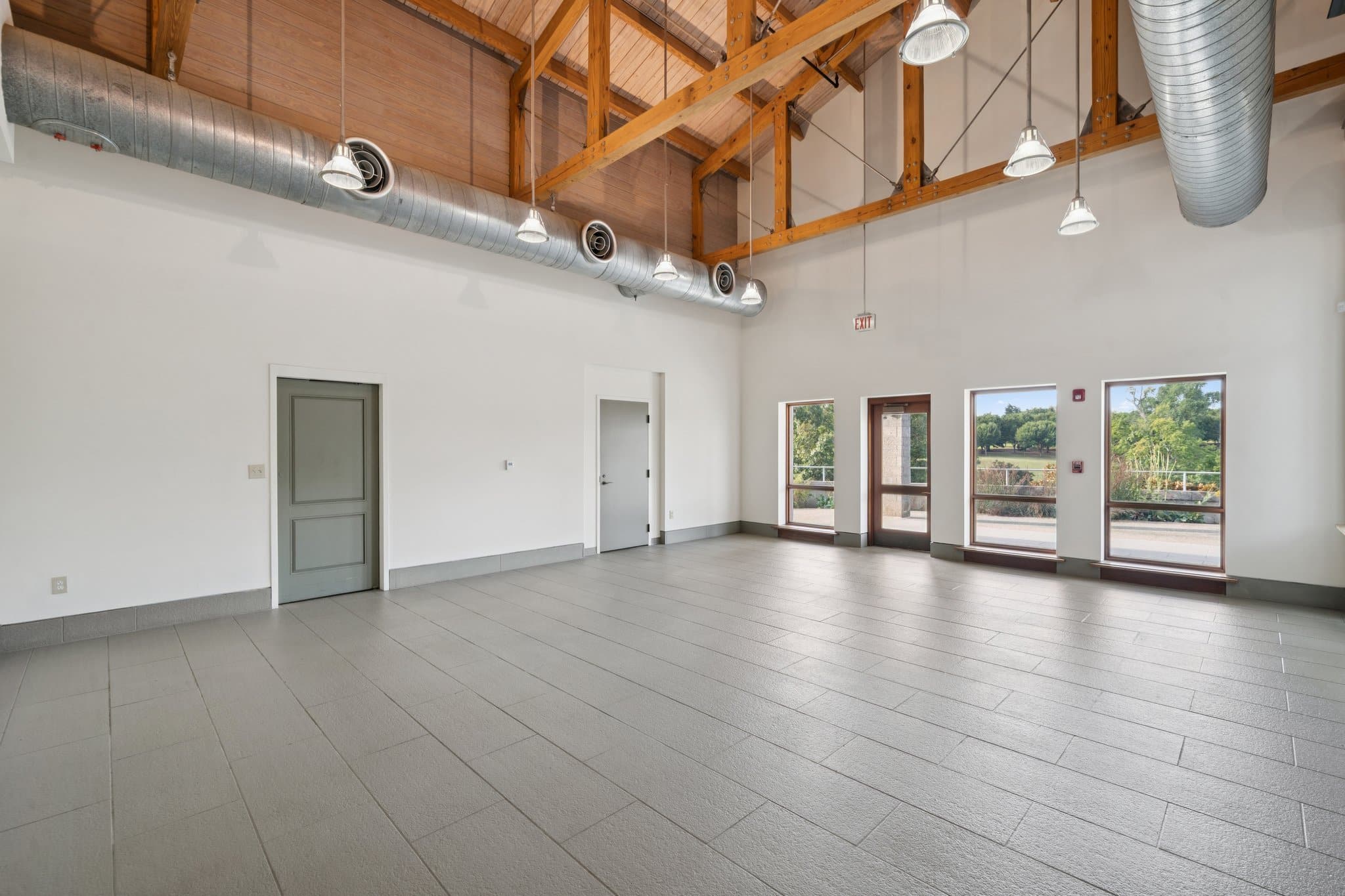 Indoor view of a room with high ceilings and exposed wooden beams, with windows looking onto a patio.