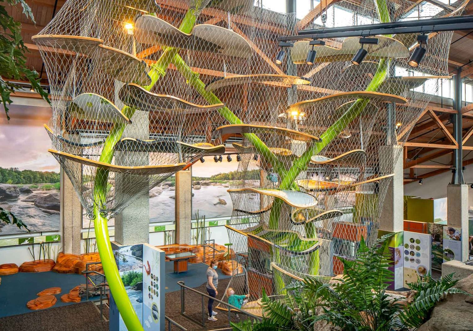 Inside a nature center with a 34-foot play structure, aquarium tanks below it, and engaging play areas. Plus a mural of the James River on the back wall.